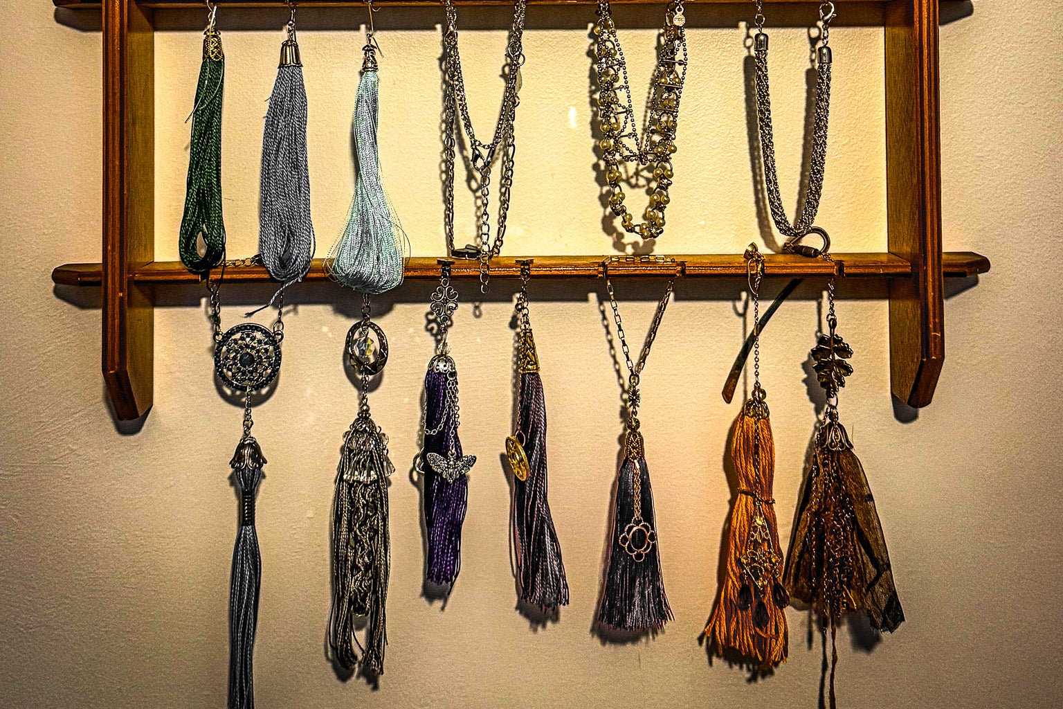 Wooden jewelry rack with various necklaces and tassels hanging on a wall.
